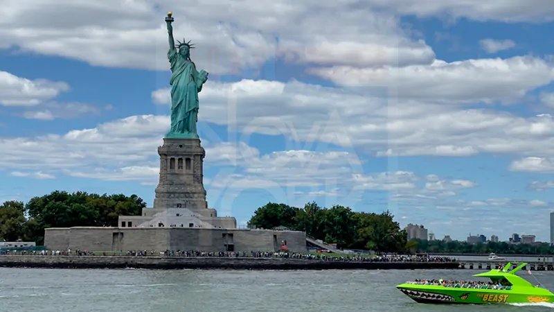 Estátua da Liberdade ao fundo com um barco verde passando na lateral direita da tela.